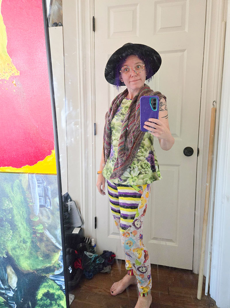 Quinn with wet purple hair, a hat, enby Animal Crossing pants, and a cactus tank top, taking a selfie in the mirror